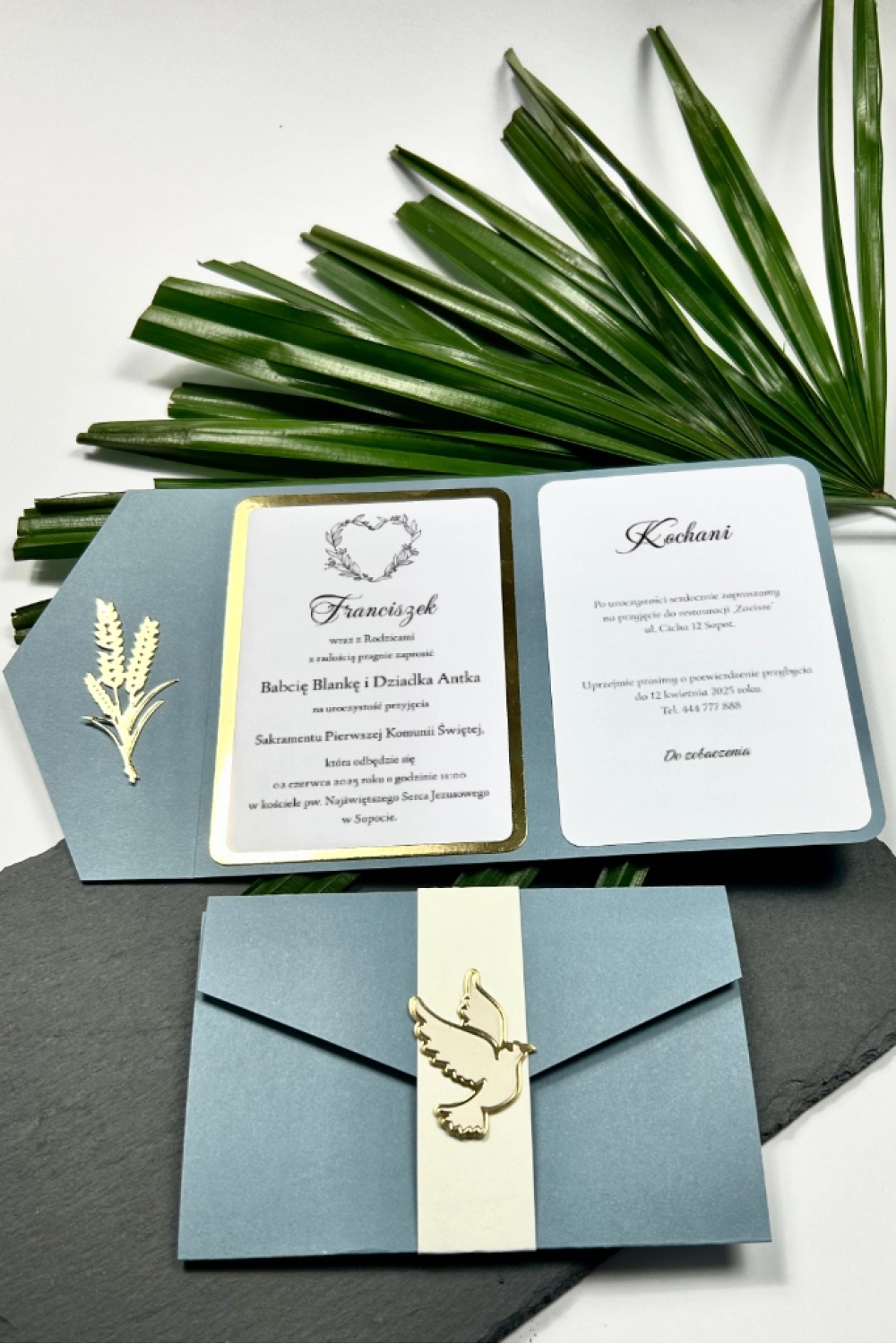 Eleganckie zaproszenie na Pierwszą Komunię Świętą w niebieskim kolorze, z otwartą kopertą i złotymi detalami.